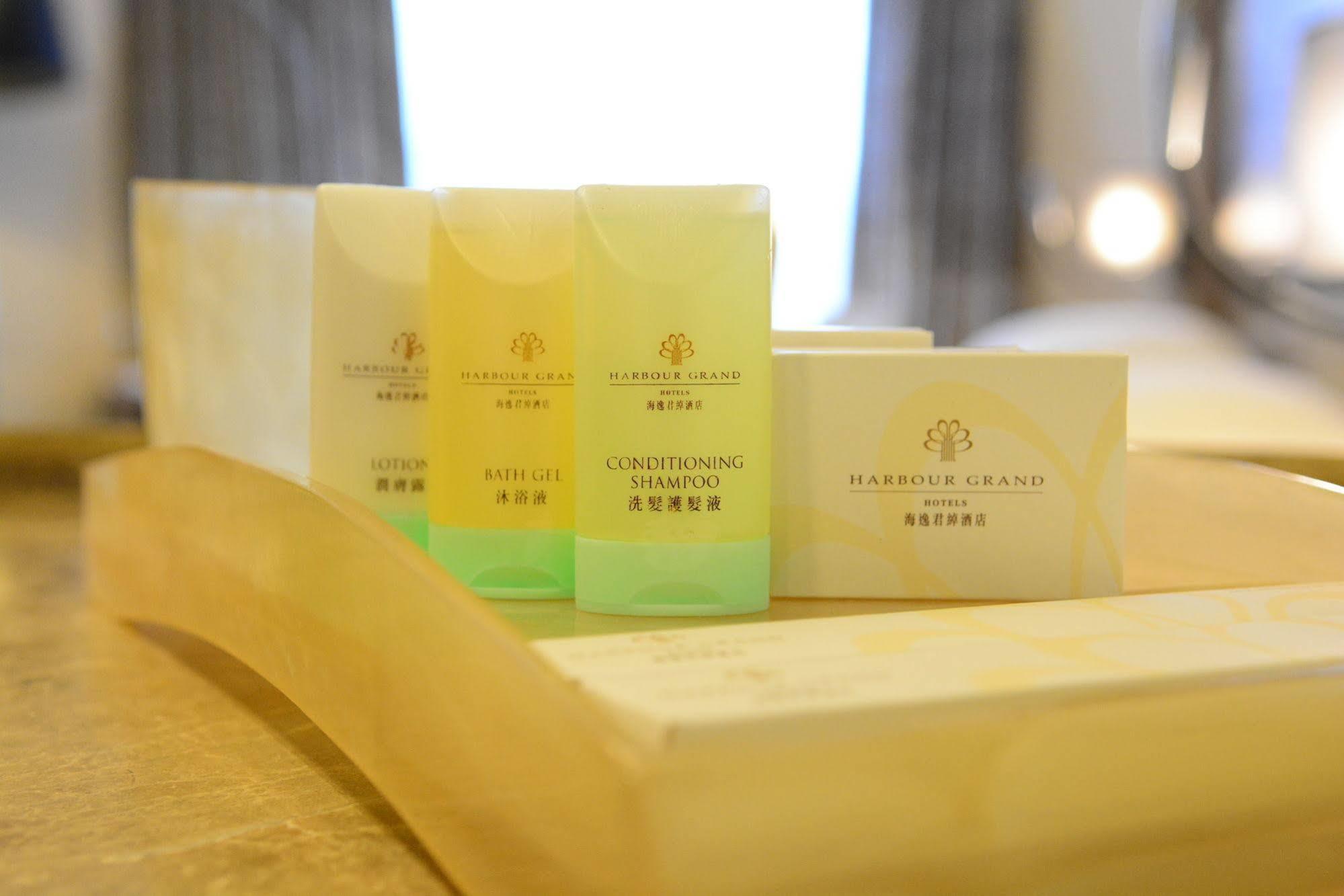 Harbour Grand Hong Kong Hotell Eksteriør bilde The photo shows a selection of personal care products arranged on a wooden tray. There are three small bottles in various colors: one yellow, one green, and one yellowish-green, labeled as "Conditioning Shampoo" and "Shampoo." Additionally, there is 